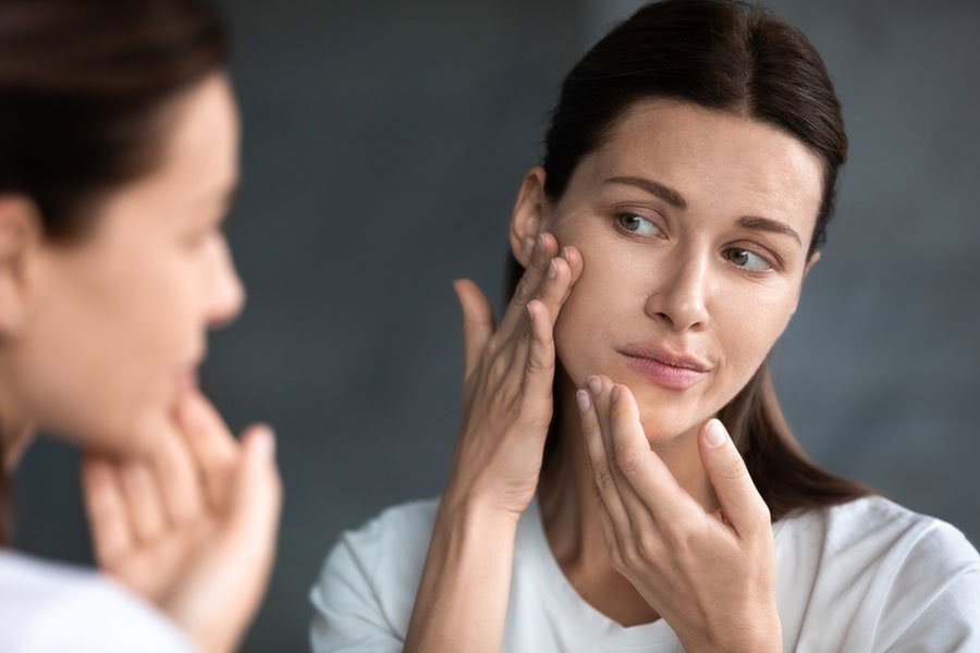 Gros plan sur une femme triste et malheureuse regardant des taches d'acné rouges sur le menton dans un miroir, contrariée par une jeune femme insatisfaite par une peau malsaine, touchant, vérifiant la peau sèche et irritée du visage, les soins de la peau et le concept de traitement