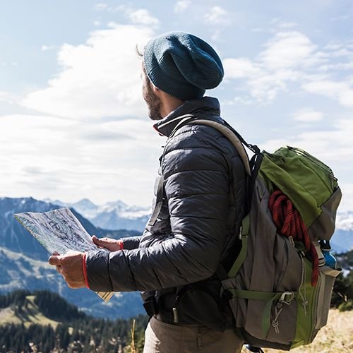 Homme avec chapeau à l'extérieur tenant une carte et regardant les montagnes