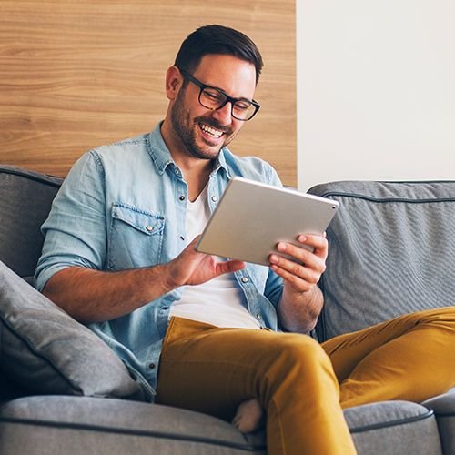 Homme, à, lunettes, sur, divan, utilisation, tablette, et, sourire