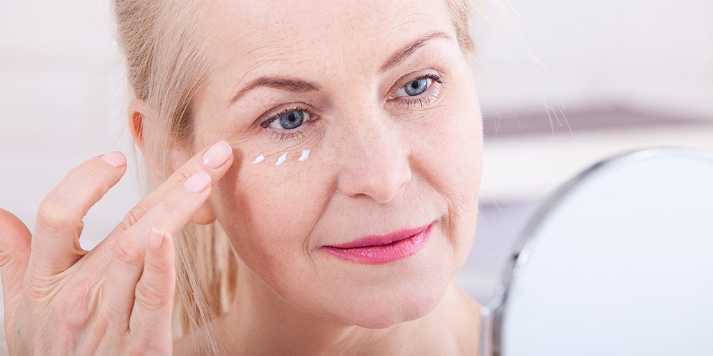 woman applying eye cream in mirror